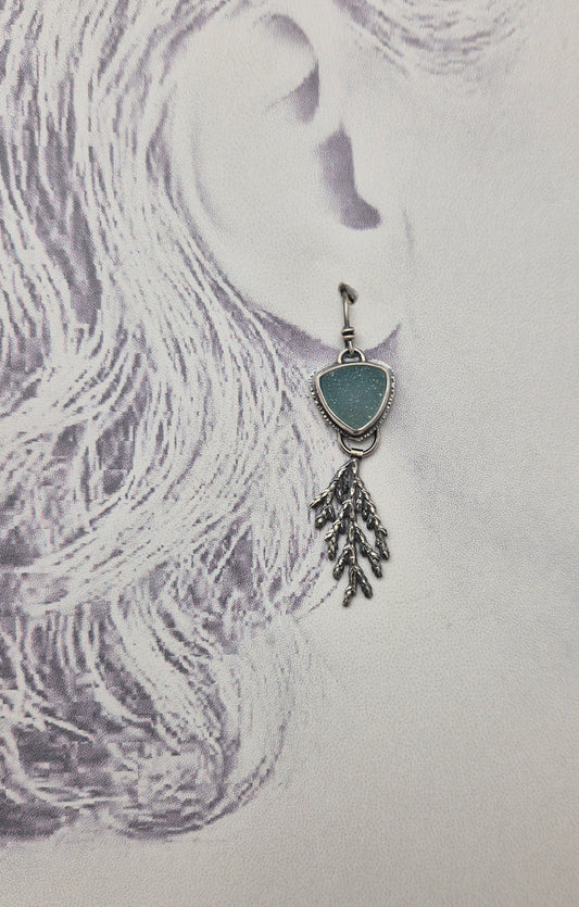 Teardrop-shaped earring with a blue stone and silver chain on a textured white background